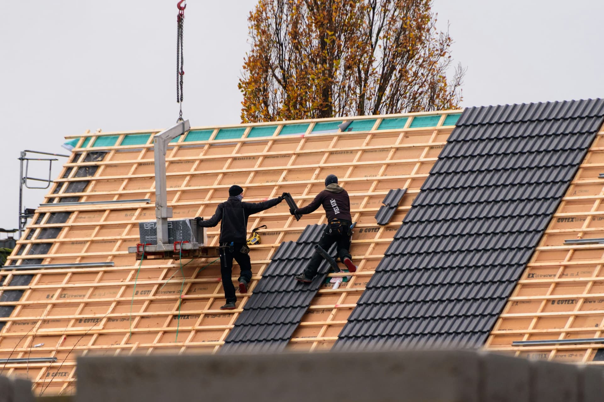 Deux couvreurs posant des tuiles sur une toiture neuve, liteaux et isolant visibles